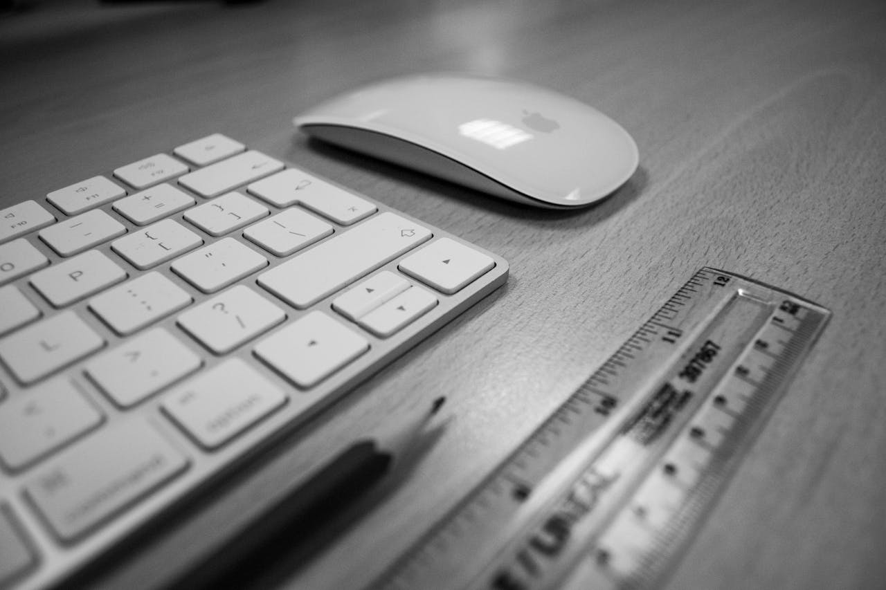 Black and white close-up of a clean, organized desk with keyboard, mouse, ruler, and pencil.